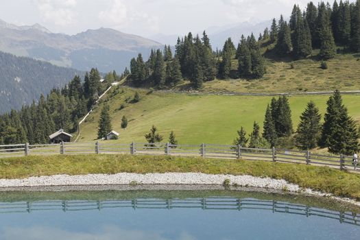 Scenic view to small alpine lake and big mountains with glacier in sunlight. Awesome green landscape with blue mountain lake among mosses in green highland valley in sunny day. Wonderful scenery.