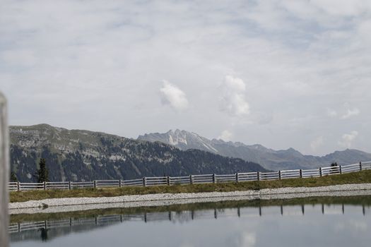 Scenic view to small alpine lake and big mountains with glacier in sunlight. Awesome green landscape with blue mountain lake among mosses in green highland valley in sunny day. Wonderful scenery.