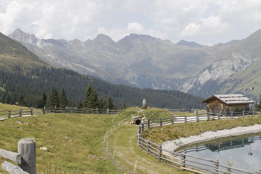 Scenic view to small alpine lake and big mountains with glacier in sunlight. Awesome green landscape with blue mountain lake among mosses in green highland valley in sunny day. Wonderful scenery.