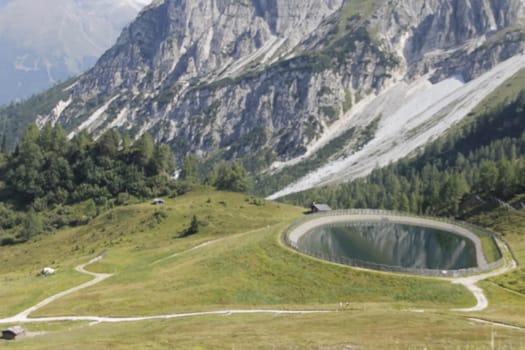 Scenic view to small alpine lake and big mountains with glacier in sunlight. Awesome green landscape with blue mountain lake among mosses in green highland valley in sunny day. Wonderful scenery.