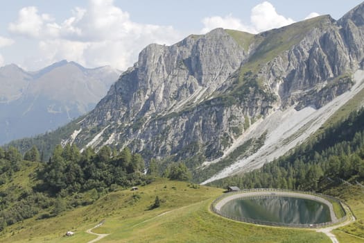 Scenic view to small alpine lake and big mountains with glacier in sunlight. Awesome green landscape with blue mountain lake among mosses in green highland valley in sunny day. Wonderful scenery.