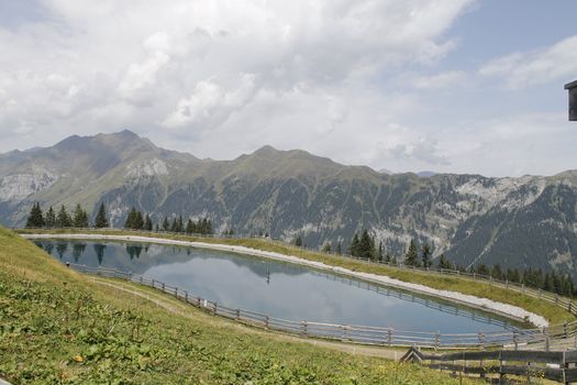 Scenic view to small alpine lake and big mountains with glacier in sunlight. Awesome green landscape with blue mountain lake among mosses in green highland valley in sunny day. Wonderful scenery.