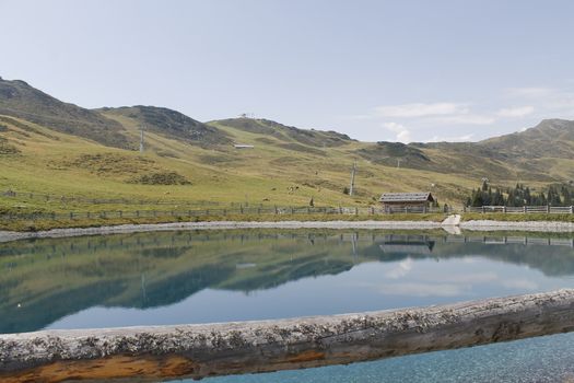 Scenic view to small alpine lake and big mountains with glacier in sunlight. Awesome green landscape with blue mountain lake among mosses in green highland valley in sunny day. Wonderful scenery.