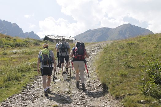 Mountain climbing. Three people go uphill with trekking poles and backpacks.