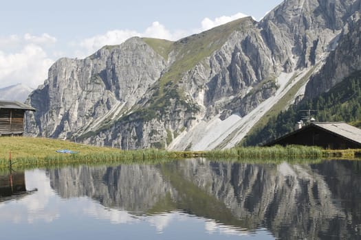 Scenic view to small alpine lake and big mountains with glacier in sunlight. Awesome green landscape with blue mountain lake among mosses in green highland valley in sunny day. Wonderful scenery.