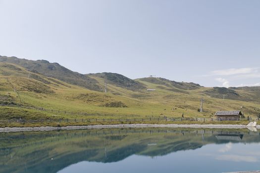 Scenic view to small alpine lake and big mountains with glacier in sunlight. Awesome green landscape with blue mountain lake among mosses in green highland valley in sunny day. Wonderful scenery.