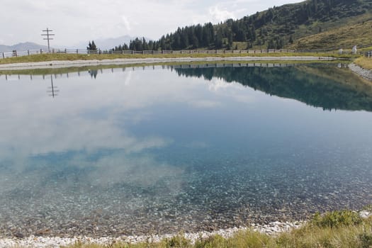 Scenic view to small alpine lake and big mountains with glacier in sunlight. Awesome green landscape with blue mountain lake among mosses in green highland valley in sunny day. Wonderful scenery.