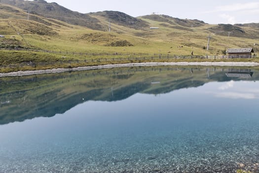 Scenic view to small alpine lake and big mountains with glacier in sunlight. Awesome green landscape with blue mountain lake among mosses in green highland valley in sunny day. Wonderful scenery.