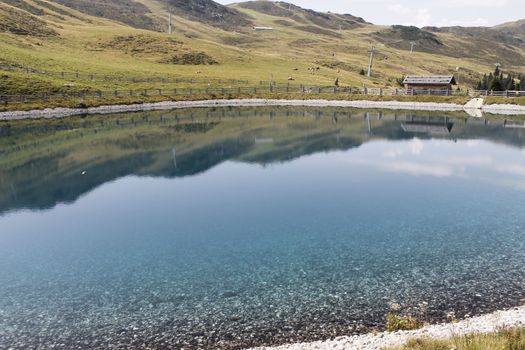 Scenic view to small alpine lake and big mountains with glacier in sunlight. Awesome green landscape with blue mountain lake among mosses in green highland valley in sunny day. Wonderful scenery.