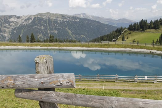 Scenic view to small alpine lake and big mountains with glacier in sunlight. Awesome green landscape with blue mountain lake among mosses in green highland valley in sunny day. Wonderful scenery.