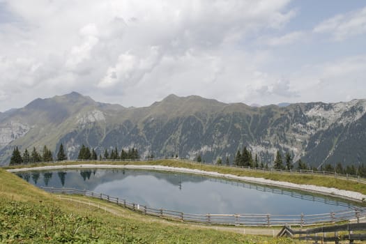 Scenic view to small alpine lake and big mountains with glacier in sunlight. Awesome green landscape with blue mountain lake among mosses in green highland valley in sunny day. Wonderful scenery.