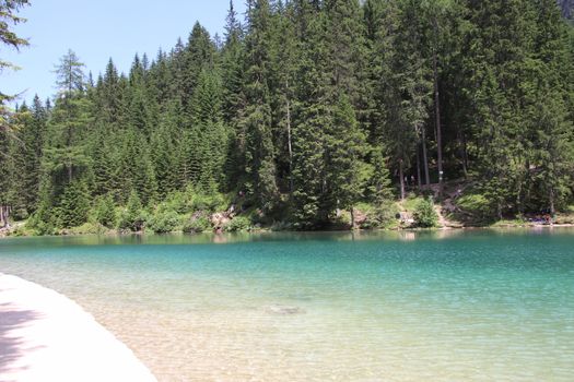 Braies Lake in Dolomites mountains forest trail in background, Sudtirol, Italy. Lake Braies is also known as Lago di Braies. The lake is surrounded by forest which are famous for scenic hiking trails.