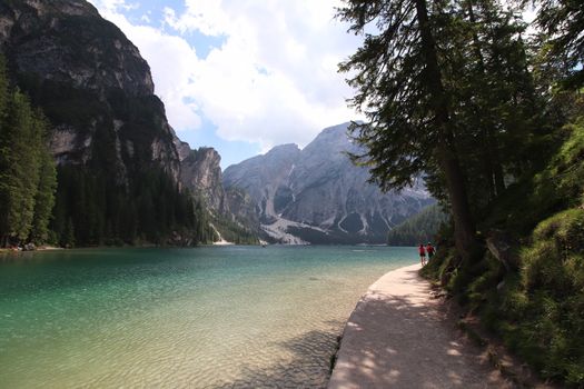 Braies Lake in Dolomites mountains forest trail in background, Sudtirol, Italy. Lake Braies is also known as Lago di Braies. The lake is surrounded by forest which are famous for scenic hiking trails.