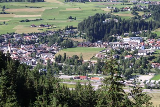 Aerial view of huge valley of the mountains of Italy, Trentino, green meadows, Slopes with green spruce trees, Dolomites on background, The town in the bottom of a valley