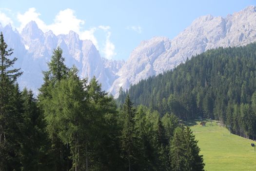 Aerial view of huge valley of the mountains of Italy, Trentino, green meadows, Slopes with green spruce trees, Dolomites on background, The town in the bottom of a valley