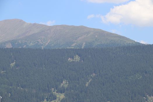 Aerial view of huge valley of the mountains of Italy, Trentino, green meadows, Slopes with green spruce trees, Dolomites on background, The town in the bottom of a valley