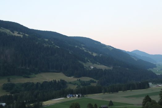 Aerial view of huge valley of the mountains of Italy, Trentino, green meadows, Slopes with green spruce trees, Dolomites on background, The town in the bottom of a valley