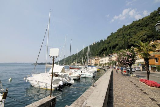 View on sailing yacht and boats parked on crystal clear blue water of amazing lake Garda and Toscolano Maderno cityscape on the background