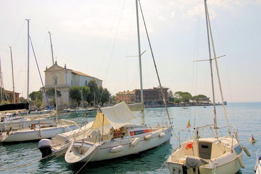 View on sailing yacht and boats parked on crystal clear blue water of amazing lake Garda and Toscolano Maderno cityscape on the background