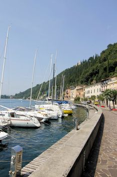 View on sailing yacht and boats parked on crystal clear blue water of amazing lake Garda and Toscolano Maderno cityscape on the background