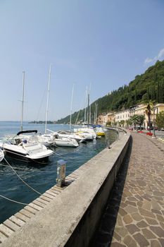 View on sailing yacht and boats parked on crystal clear blue water of amazing lake Garda and Toscolano Maderno cityscape on the background