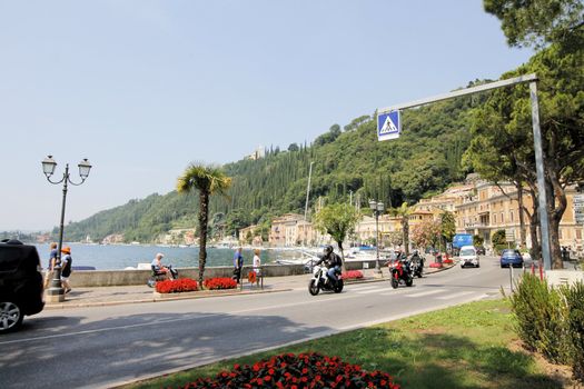 Scenic panoramic beltway road around lake Garda with medieval architecture buildings and rich northern Italy trees and plants growing on coast