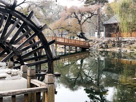 Water mill wheel in a calm little river and little pavilion on the background at The Imperial Summer Palace of The Mountain Resort in Chengde. China. 