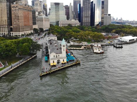 Aerial view of Battery Park pier A leading to Liberty Island, people can be seen waiting in line for boarding as well as looking at Liberty Island located opposite to the docks. October, 22nd, 2019