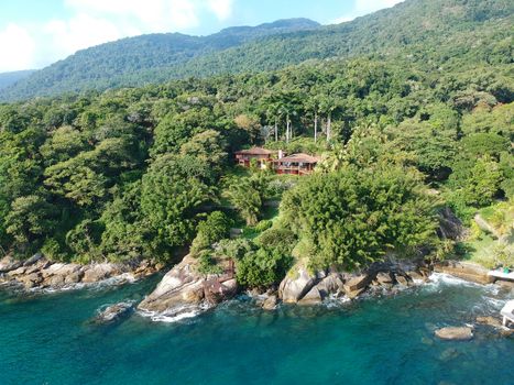 Aerial view of luxury house in tropical forest surrounded by trees and next to the ocean and blue turquoise water. luxurious villa and spacious pavilion next to the sea, Brazil.