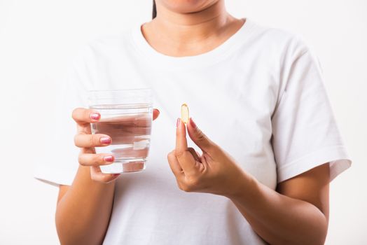 Closeup young Asian woman hold fish oil vitamin drugs in hand ready take medicines with a glass of water, studio shot isolated on white background, Healthcare and medical pharmacy concept