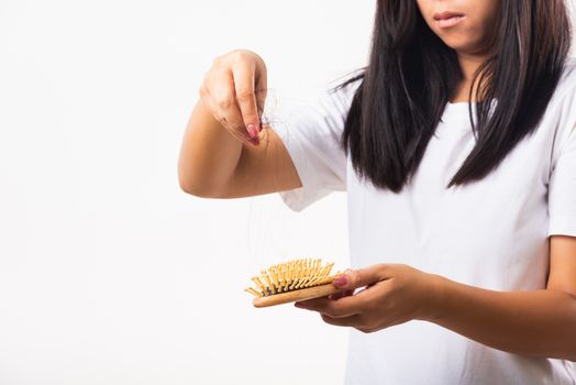 Asian woman unhappy weak hair problem her hold hairbrush with damaged long loss hair in the comb brush she pulls loss hair from the brush, isolated on white background, Medicine health care concept