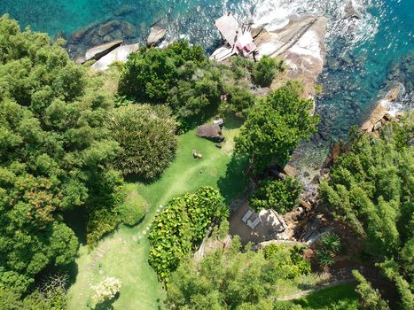 Aerial view of quiet little garden with wooden chairs between rocks and next to the ocean crystal clear water in tropical country. Brazil