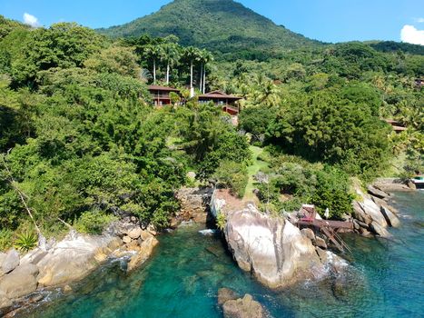 Aerial view of luxury house in tropical forest surrounded by trees and next to the ocean and blue turquoise water. luxurious villa and spacious pavilion next to the sea, Brazil.