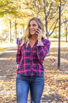 A gorgeous blonde model talks on her cellphone on an autumn day outdoors in a park