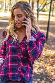 A gorgeous blonde model talks on her cellphone on an autumn day outdoors in a park