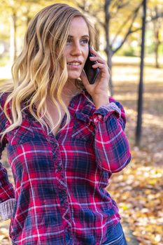 A gorgeous blonde model talks on her cellphone on an autumn day outdoors in a park