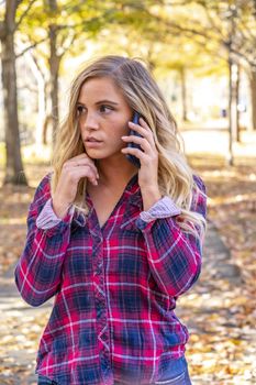 A gorgeous blonde model talks on her cellphone on an autumn day outdoors in a park