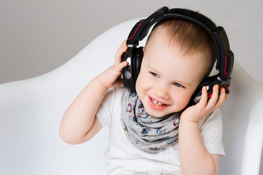 Fun and cute smiling little boy listening music in earphones and having fun. Stylish wearing in white t shirt and scarf, with blue eyes and pure skin, having fun.