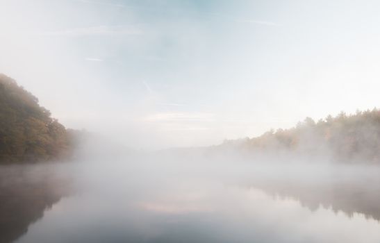 Early morning fog just above the water level partly of Connecticut River  with colorful fall foliage along both sides converging into distance.