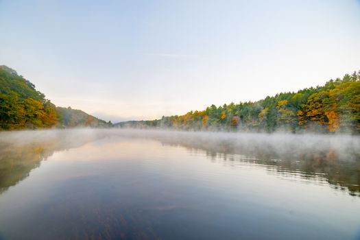 Scenic early morning fog just above the water level of Connecticut River with colorful fall foliage along both sides converging into distance.