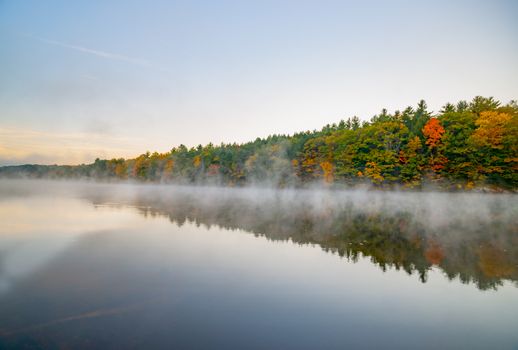 Scenic Early morning fog just above the water level of Connecticut River with colorful fall foliage reflected in calm water.