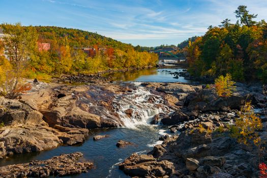Idyllic stream and Rumford Falls surrounded by beautiful forested hills and autumn foliage colors.
