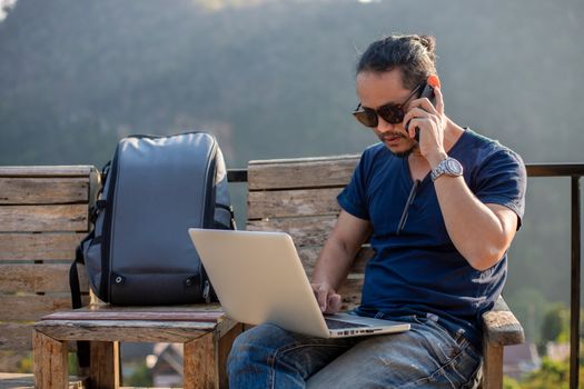 Asian men backpacks and traveler working on computer laptop at outdoor nature and He is relaxing and enjoying on travel