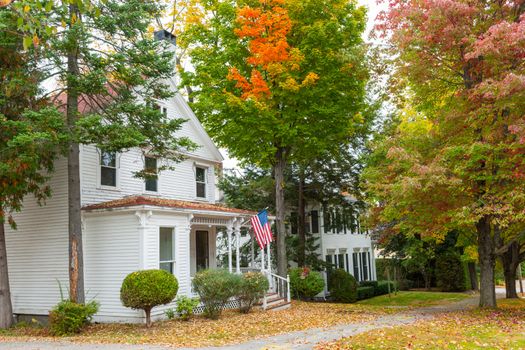 American flag flies outside  in street of residential American style homes in wooded suburb in fall with colors and leaf fall starting.