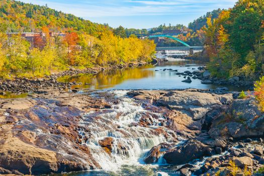 Idyllic stream with bridge and Rumford Falls surrounded by beautiful forested hills and autumn foliage colors.