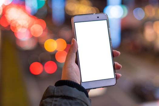 Woman holding a smartphone with a blank white screen at night with lights from car traffic in the background