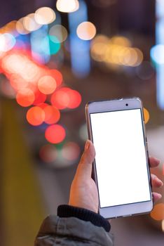 Woman holding a smartphone with a blank white screen at night with lights from car traffic in the background