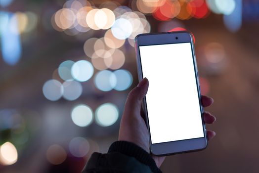 Woman holding a smartphone with a blank white screen at night with lights from car traffic in the background