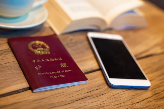 Chinese passport and smartphone on a wooden table with an open book and coffee cup in a coffee shop