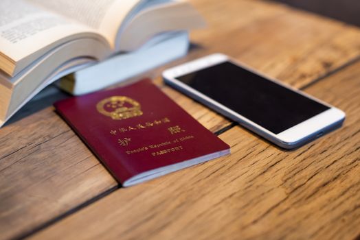 Chinese passport and smartphone on a wooden table with an open book in a coffee shop